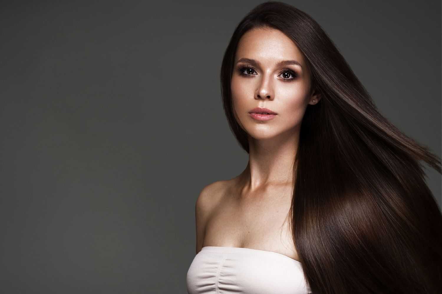 Woman with long brown hair and strapless top, facing the camera with a neutral expression.