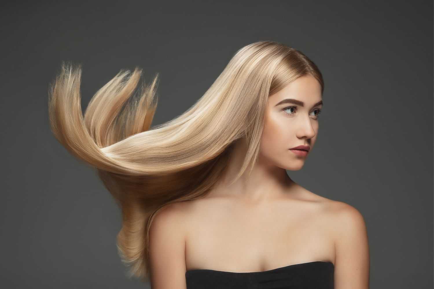 Woman with long, flowing blonde hair against a dark background, wearing a black strapless top.